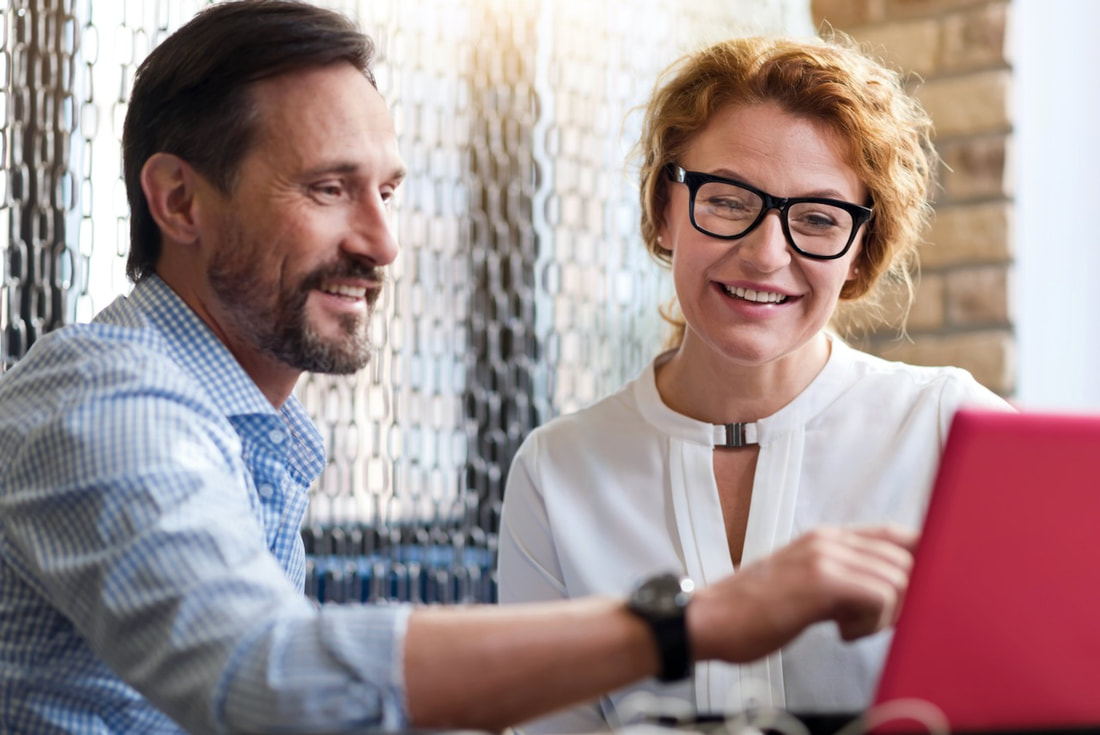 Image of a middle-aged woman and man looking a laptop and smiling as if they've found what they want. SEO will help customers find you and it's a service of 4-Good Writing.